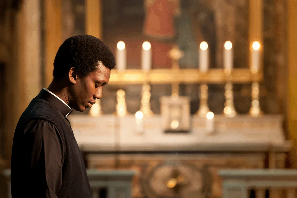 A seminarian praying before the candle-lit altar of a church